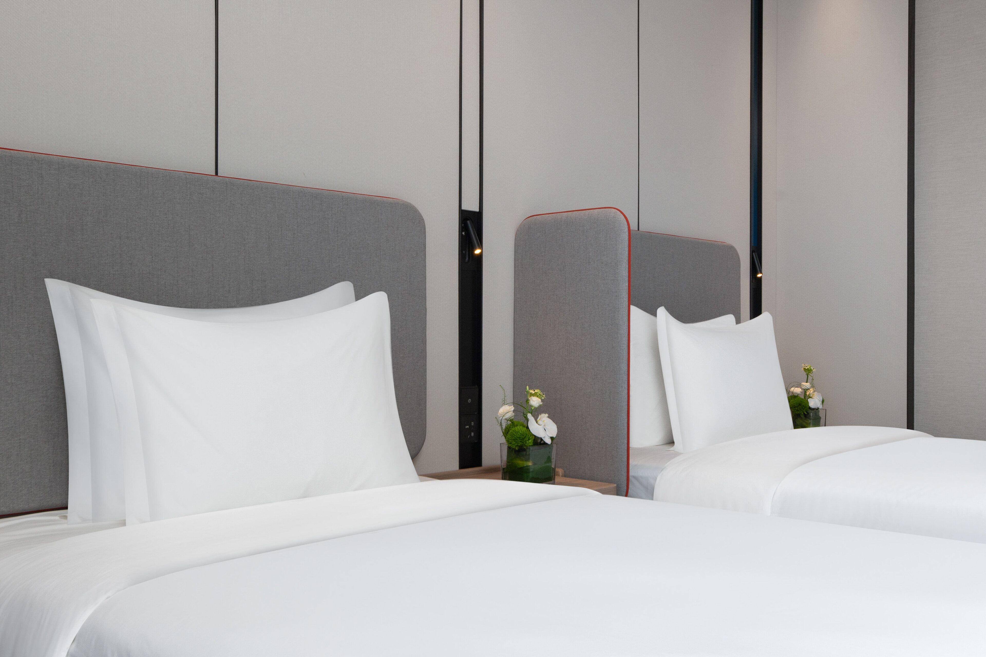 Una habitación de hotel moderna con dos camas, un espejo y un florero con flores.