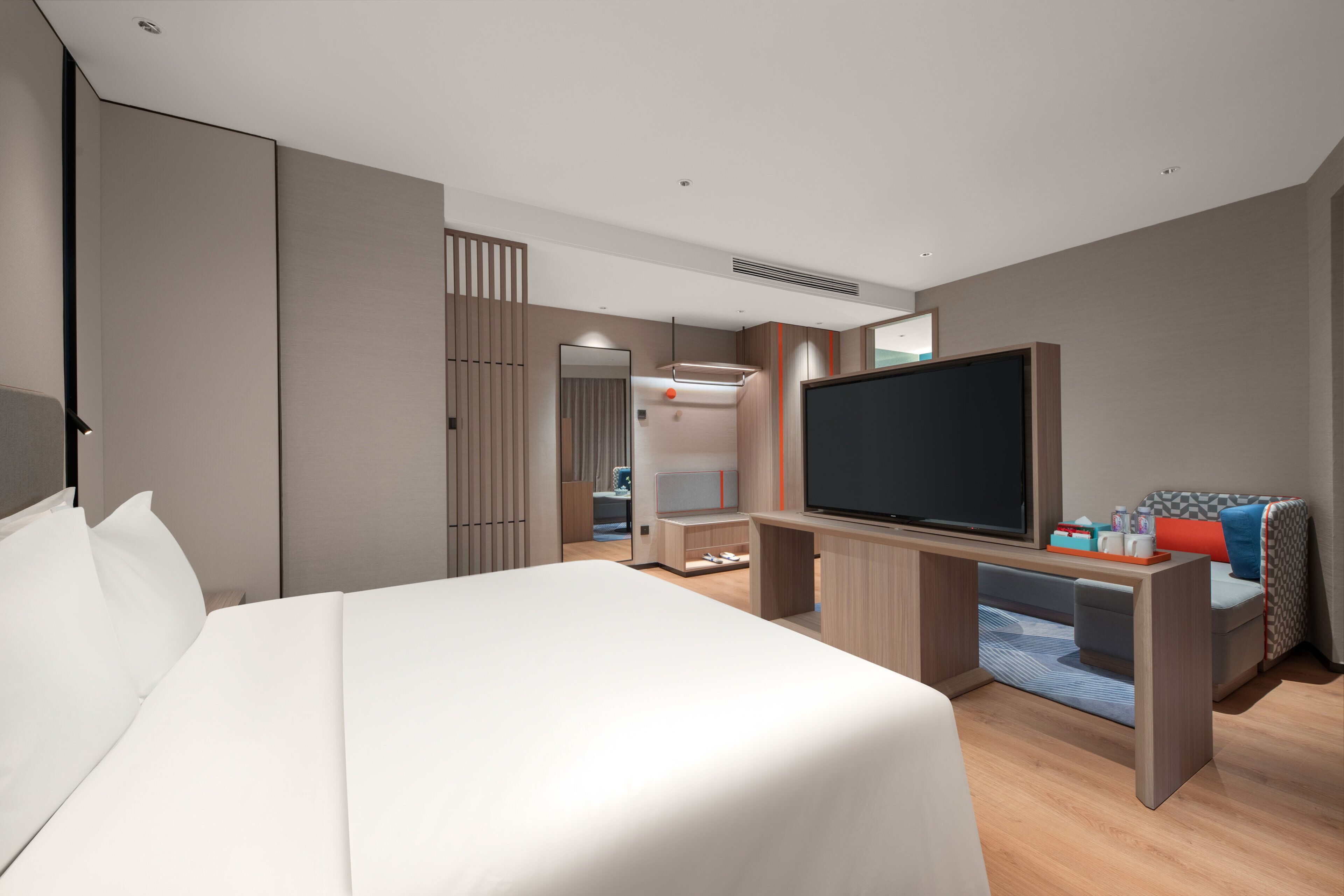 Une chambre d’hôtel moderne dotée d’un grand lit, d’une télévision à écran plat, d’un bureau avec un ordinateur et d’un coin salon comprenant un canapé et un fauteuil.