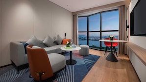 A modern hotel room with a sofa, a small round table, a red chair, and a large window offering a city view. - Holiday Inn Express Shantou Chenghai by IHG (Shantou)