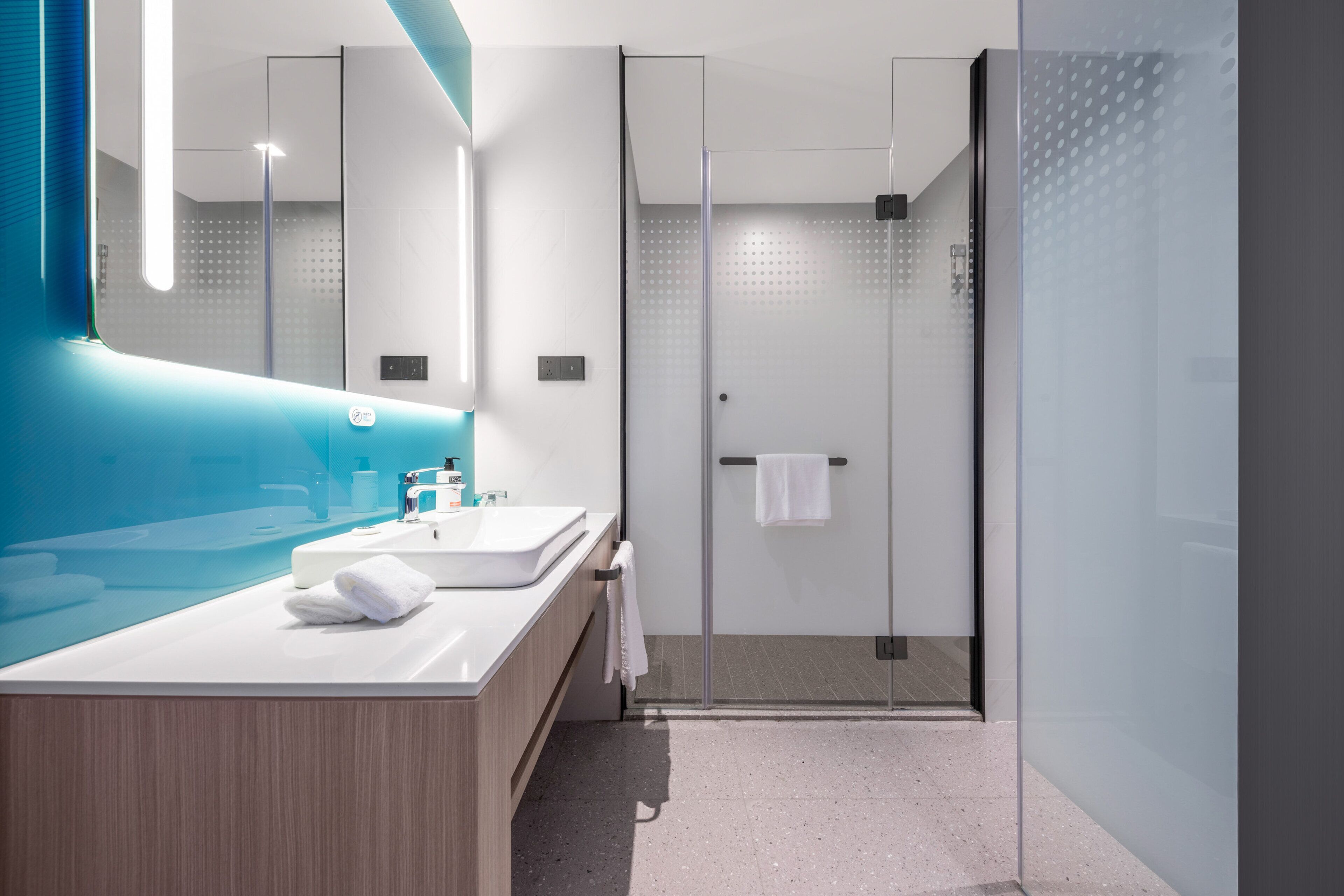 Un baño moderno con cabina de ducha de vidrio, tocador de madera y una pared de acento azul.