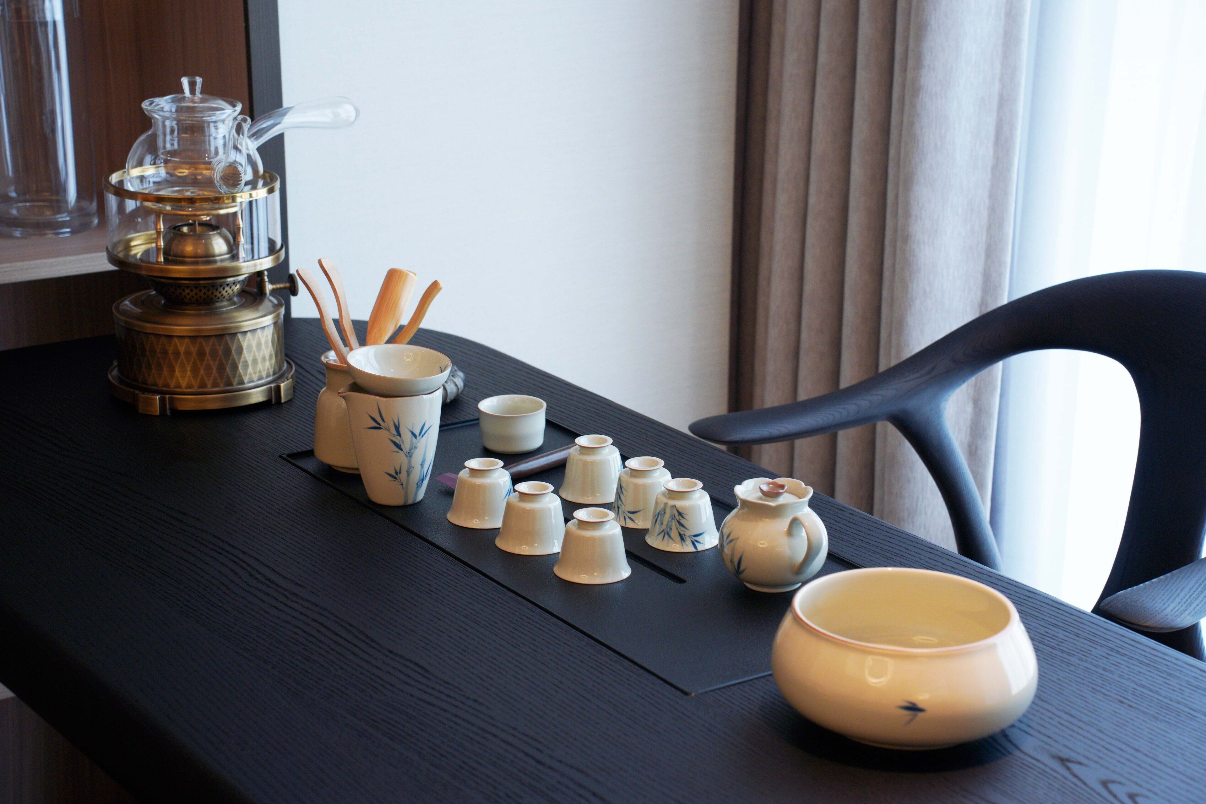 A table with a tea set, including a teapot, cups, and chopsticks, arranged on a black mat.