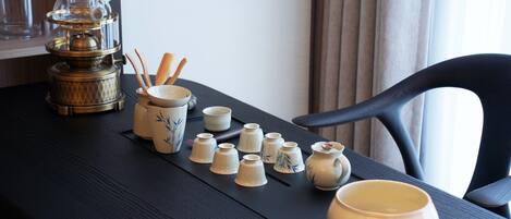 A table with a tea set, including a teapot, cups, and chopsticks, arranged on a black mat.