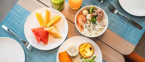 Una mesa con diversos platos, incluyendo una ensalada de sandía, un tazón de sopa y un plato con un pastel y verduras. También hay dos vasos de jugo y un tenedor sobre la mesa.