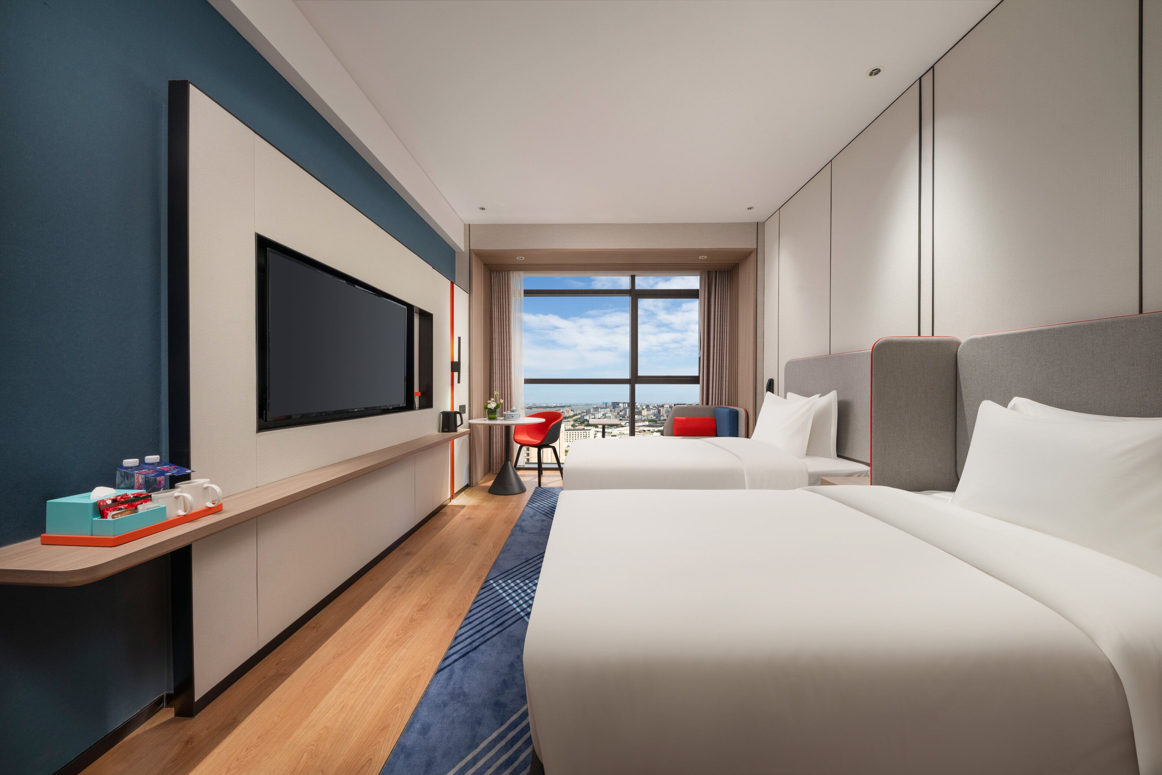Een hotelkamer met een groot bed, een bureau met stoel, een aan de muur bevestigde televisie en een raam met uitzicht op de stad.