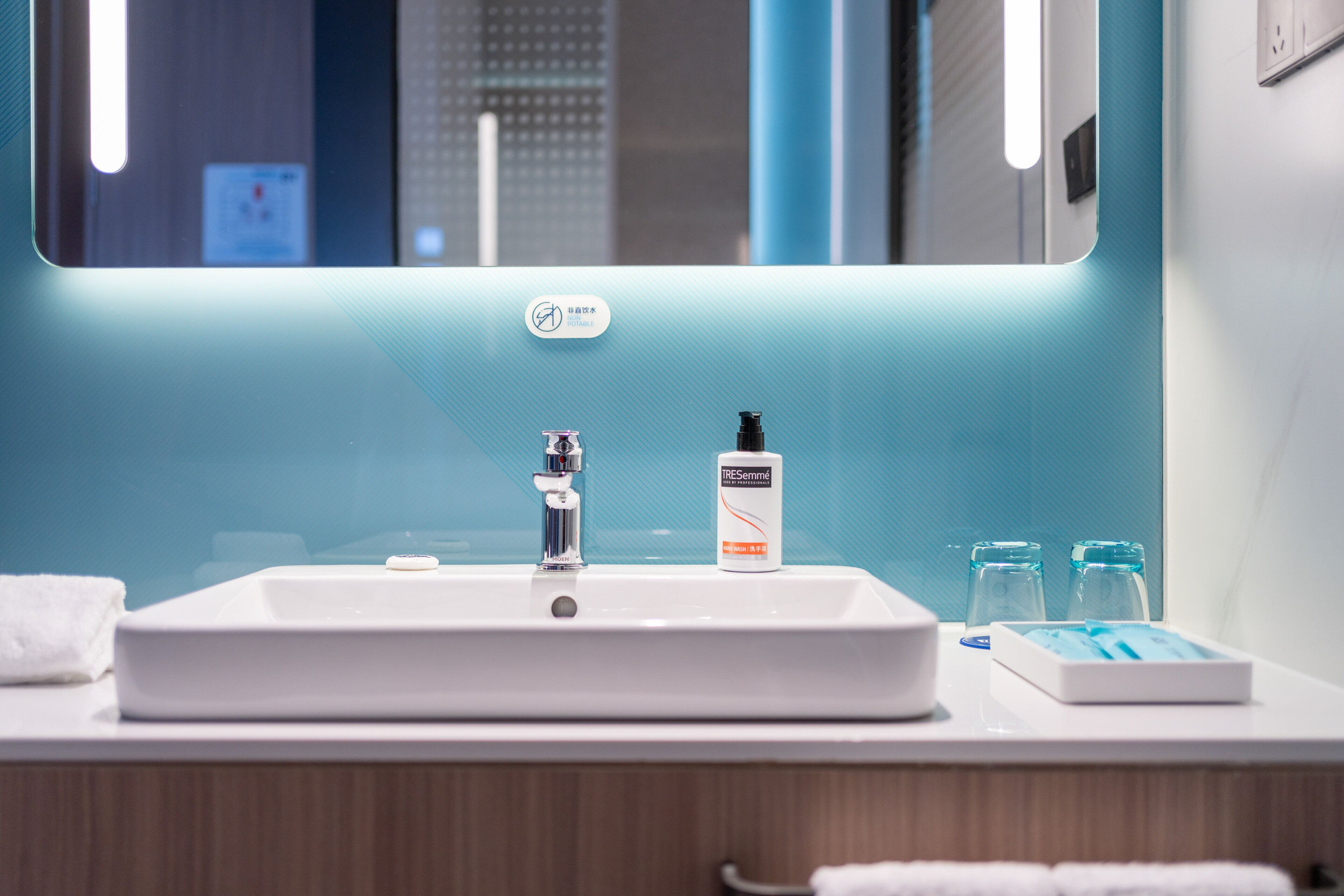 A modern bathroom with a white sink, a mirror, and a bottle of hand soap.