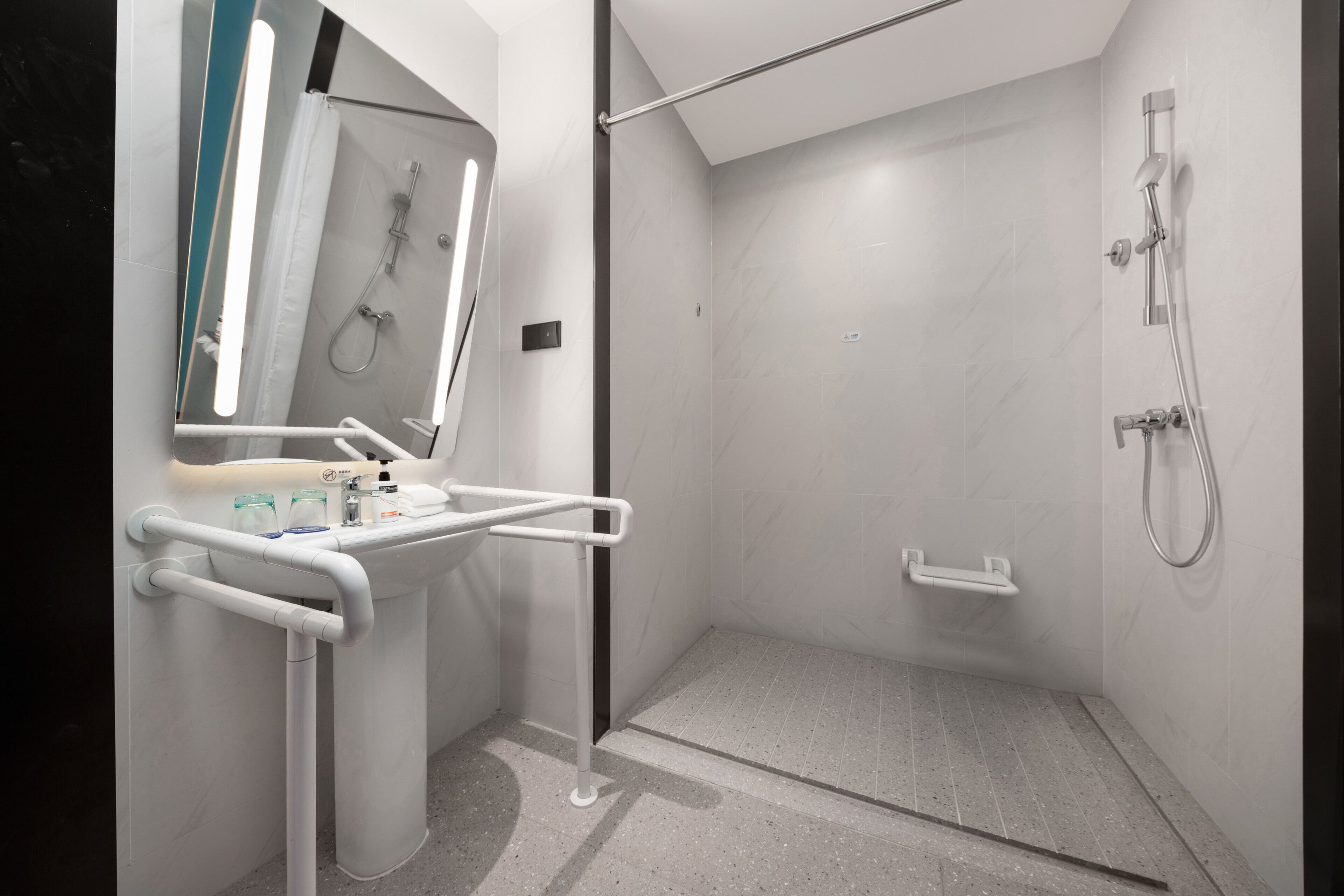 Une salle de bain moderne avec une douche à parois de verre, un lavabo blanc avec un miroir et une barre d’appui.