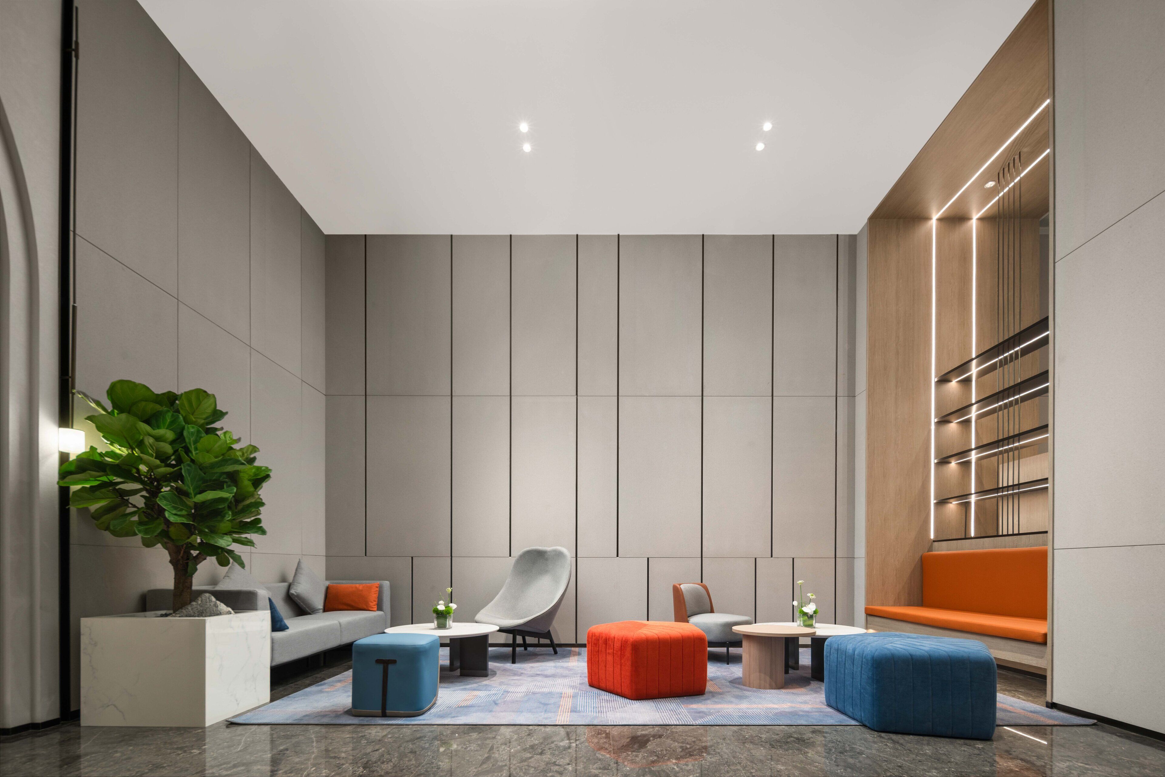 A modern lobby with a grey sofa, a blue ottoman, a grey chair, and a wooden bench.