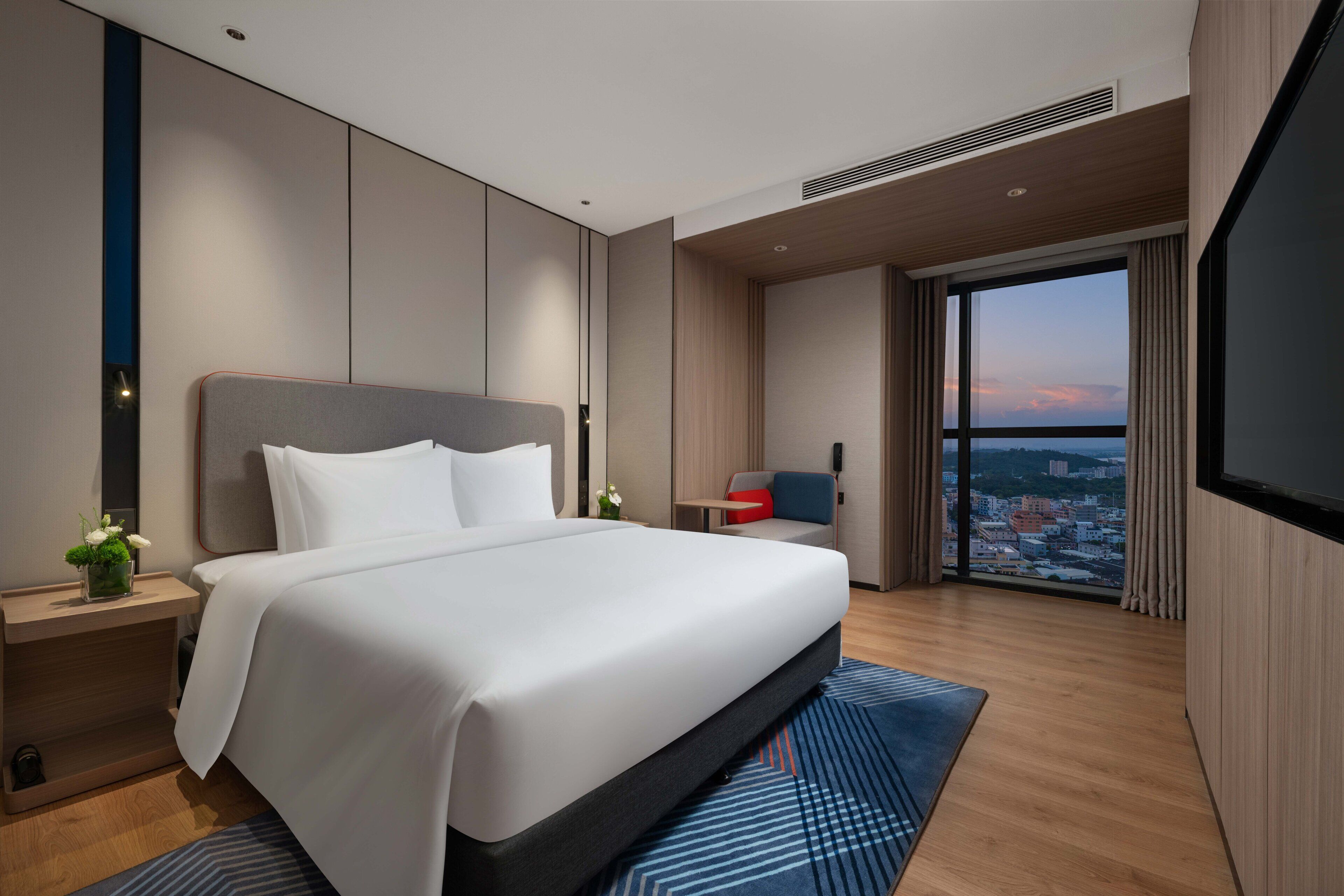 Une chambre d’hôtel moderne dotée d’un grand lit, d’un bureau, d’une chaise et d’une grande fenêtre donnant sur la ville.