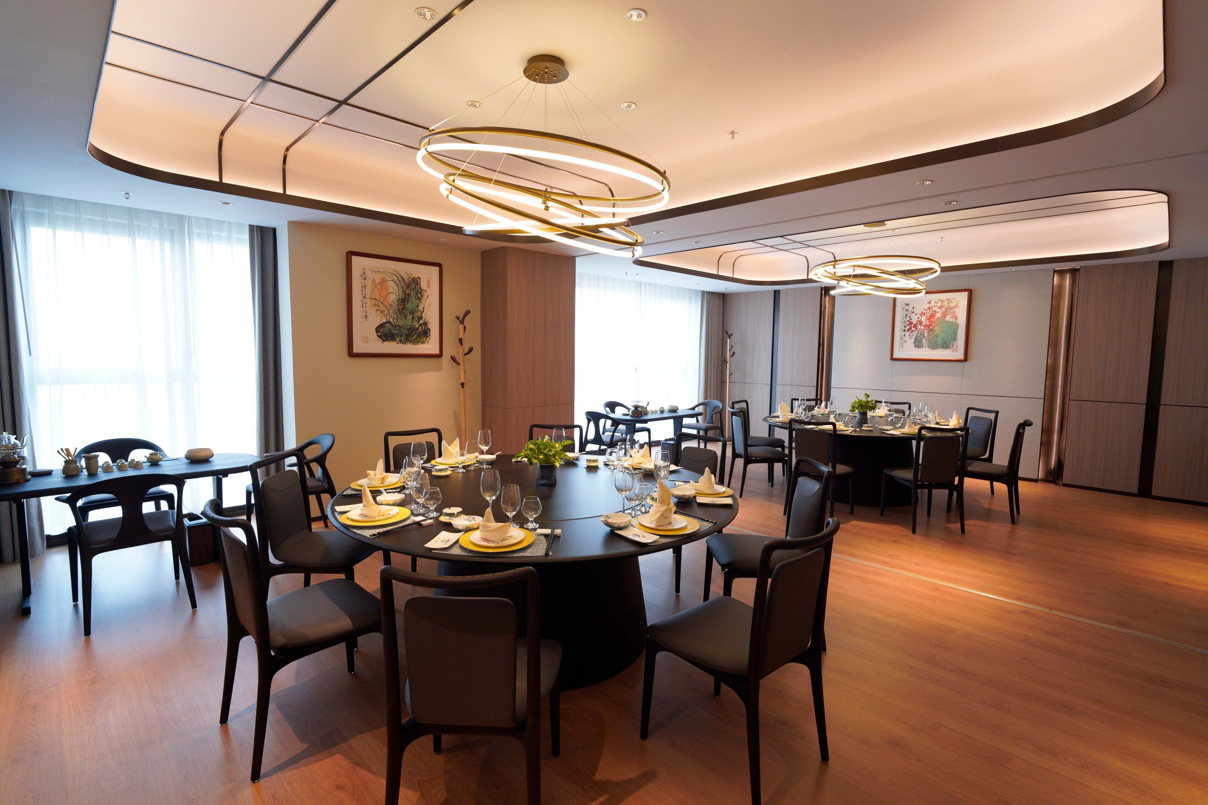A spacious dining area with round tables, black chairs, and modern lighting fixtures.
