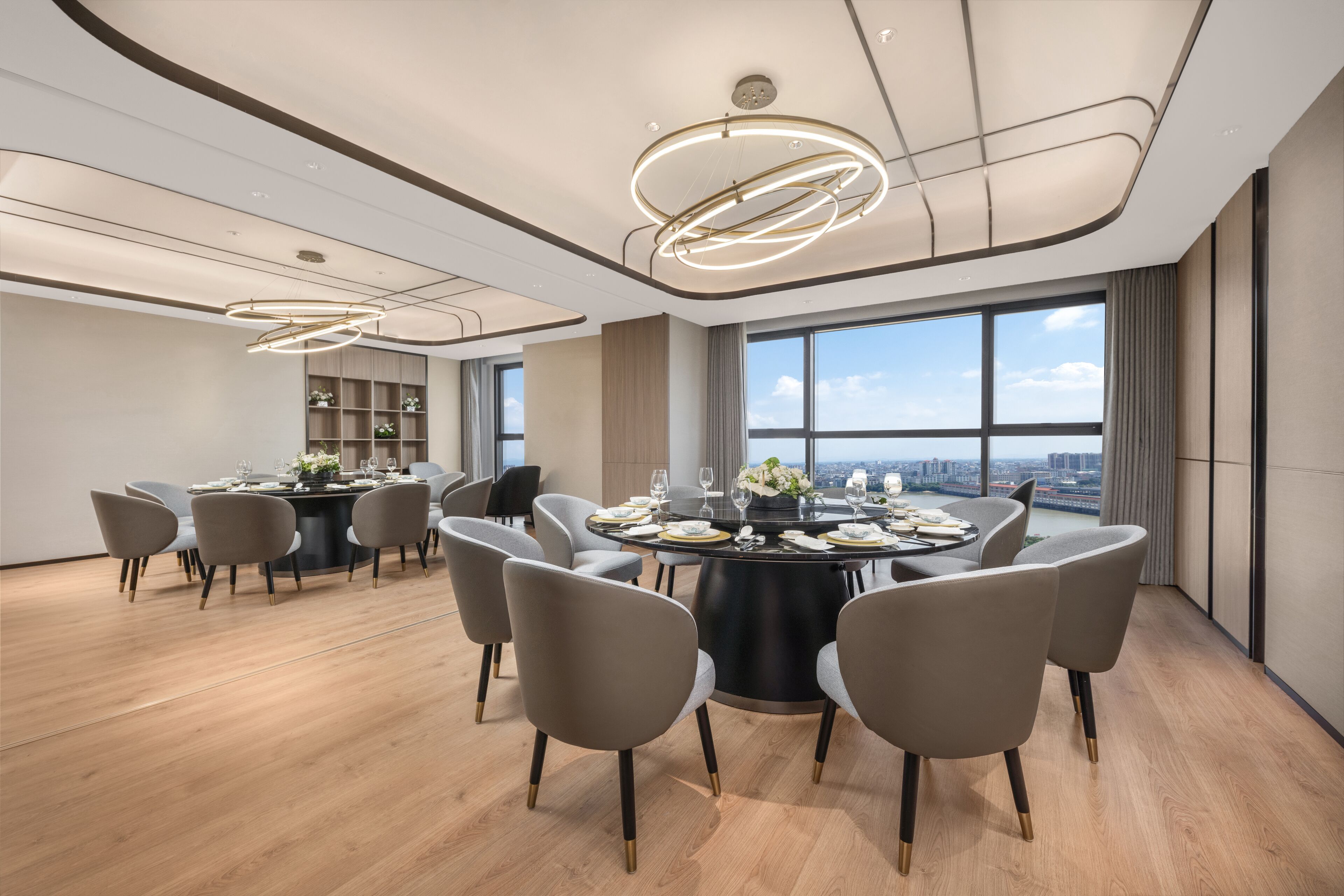 A modern dining area with a round table, grey chairs, and a city view through large windows.