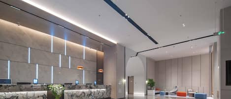 A modern hotel lobby with a marble reception desk, seating area with chairs and ottomans, and a large plant.