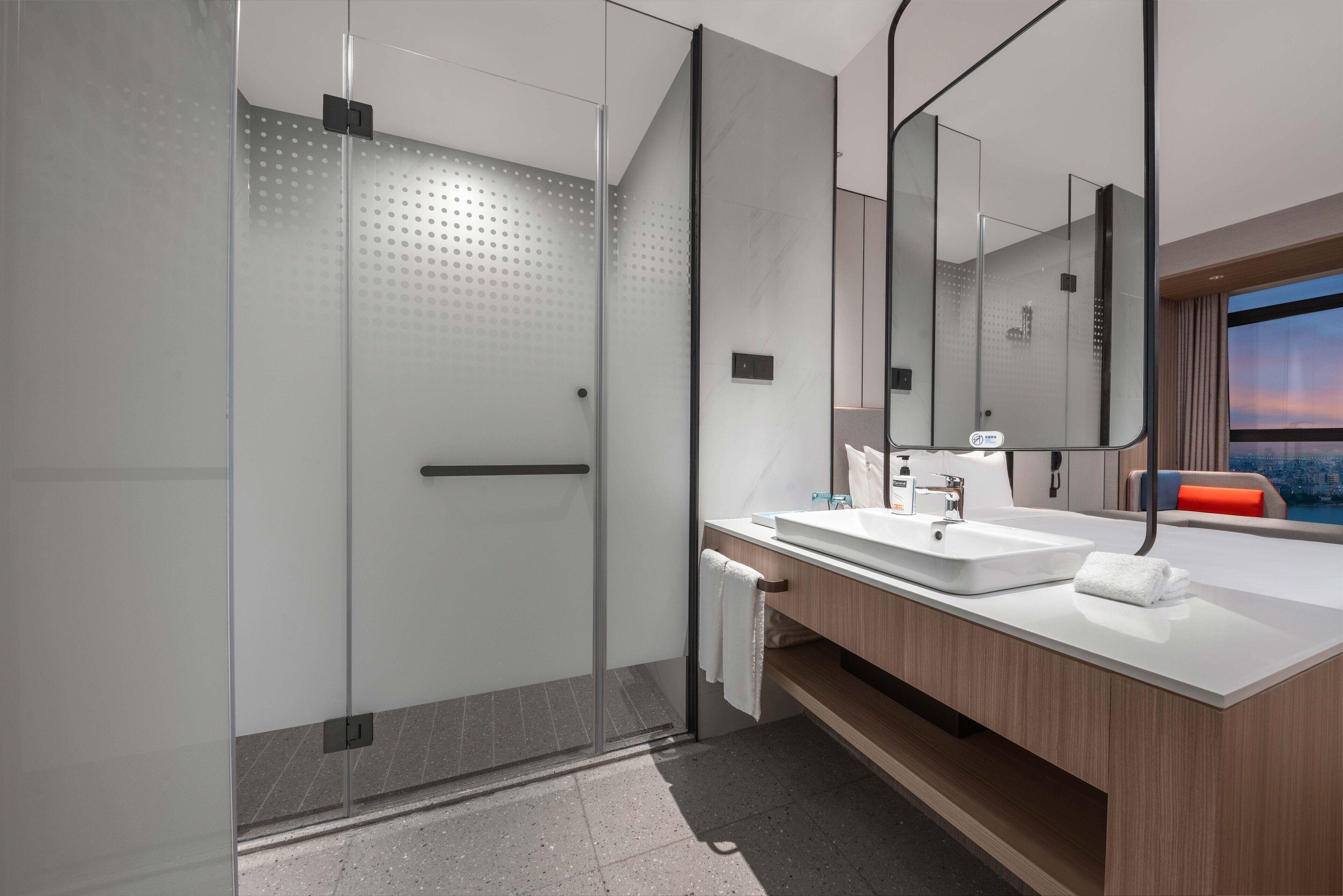 A modern bathroom with a glass-enclosed shower, a white sink, and a large mirror.