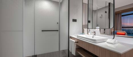 A modern bathroom with a glass-enclosed shower, a white sink, and a large mirror.