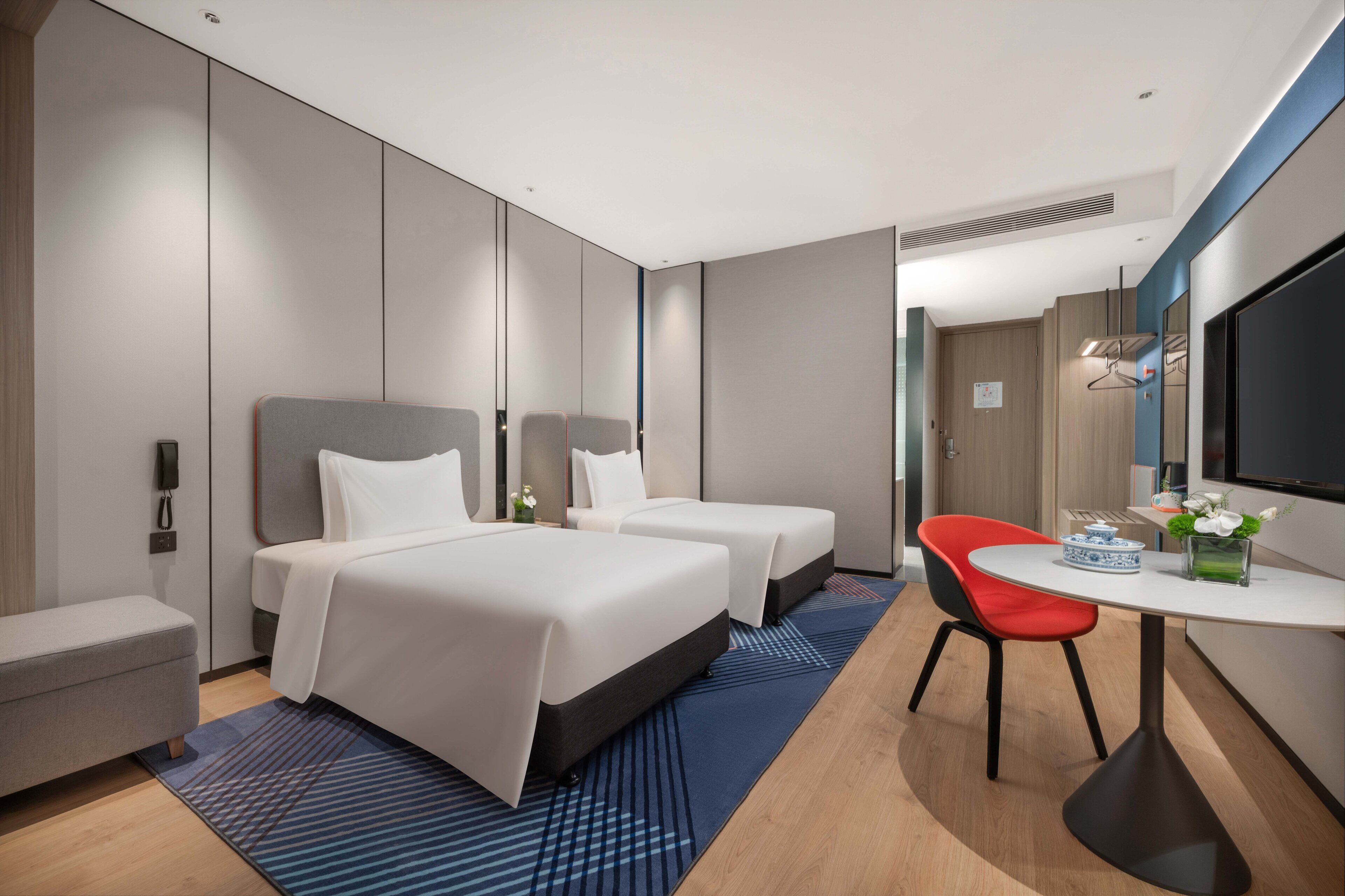 A modern hotel room with two beds, a desk, a chair, and a TV.