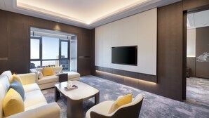 A modern living room with a large flat-screen TV mounted on the wall, a sofa set, a coffee table, and a large window offering a city view. - voco Xiongan by IHG (Baoding)