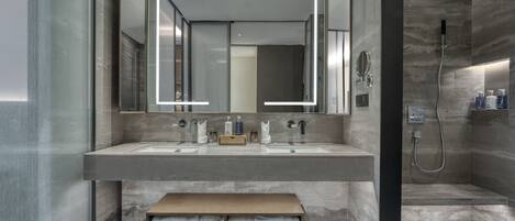 A modern bathroom with a large mirror, two sinks, a bench, and a shower area.