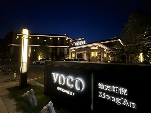 A hotel entrance with illuminated signage, a covered driveway, and a parking area.