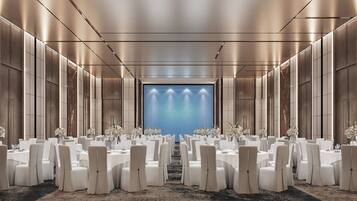 A conference room with rows of tables and chairs, a large blue screen at the end, and a modern design with metallic walls and ceiling.
