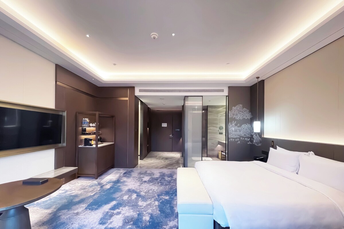 Quarto de hotel moderno com cama grande, televisão de tela plana, escrivaninha e closet espaçoso.