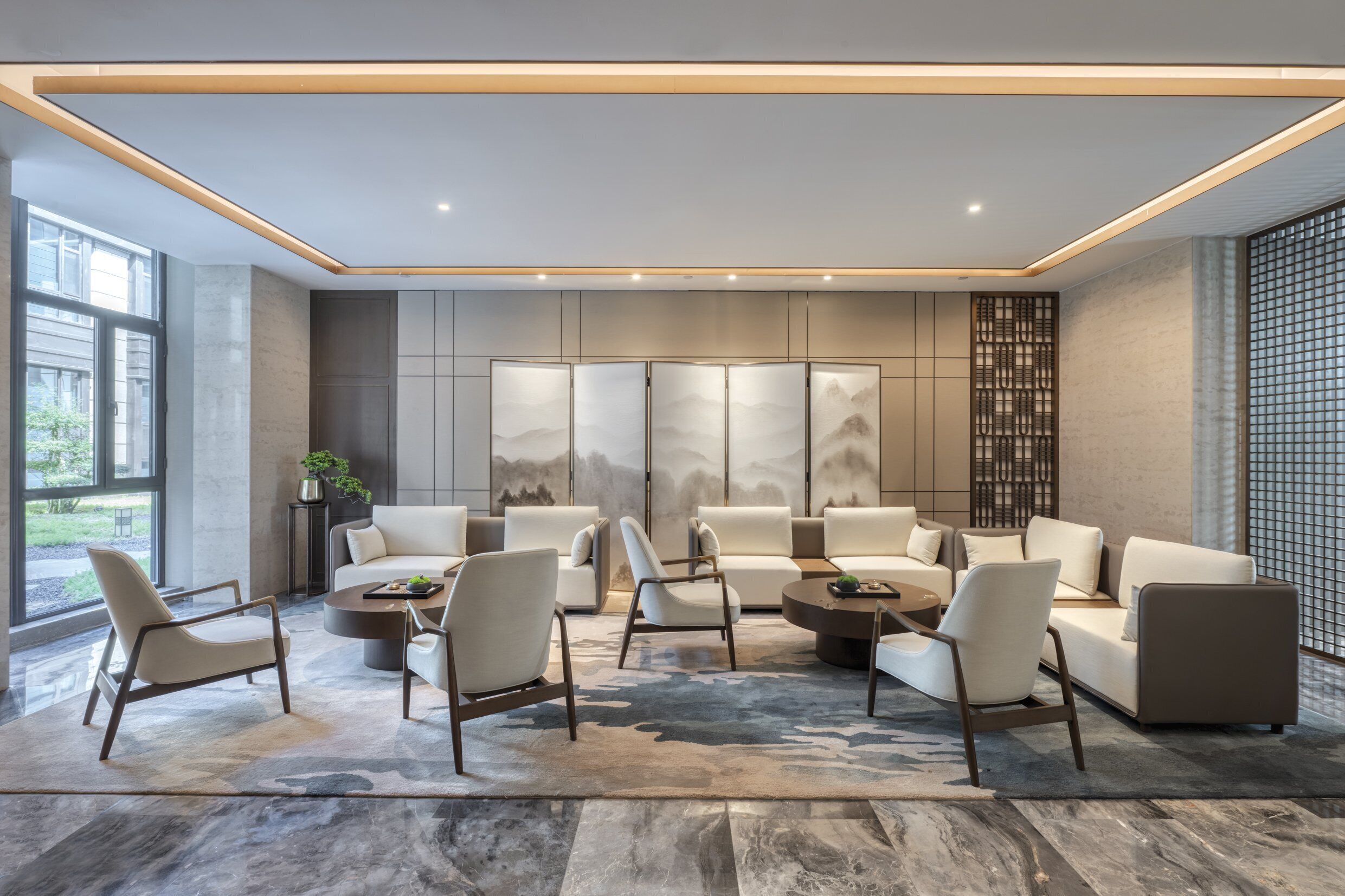 Un área de descanso moderna con sofás, sillones y una mesa de centro, que cuenta con un ventanal grande y un panel decorativo en la pared.