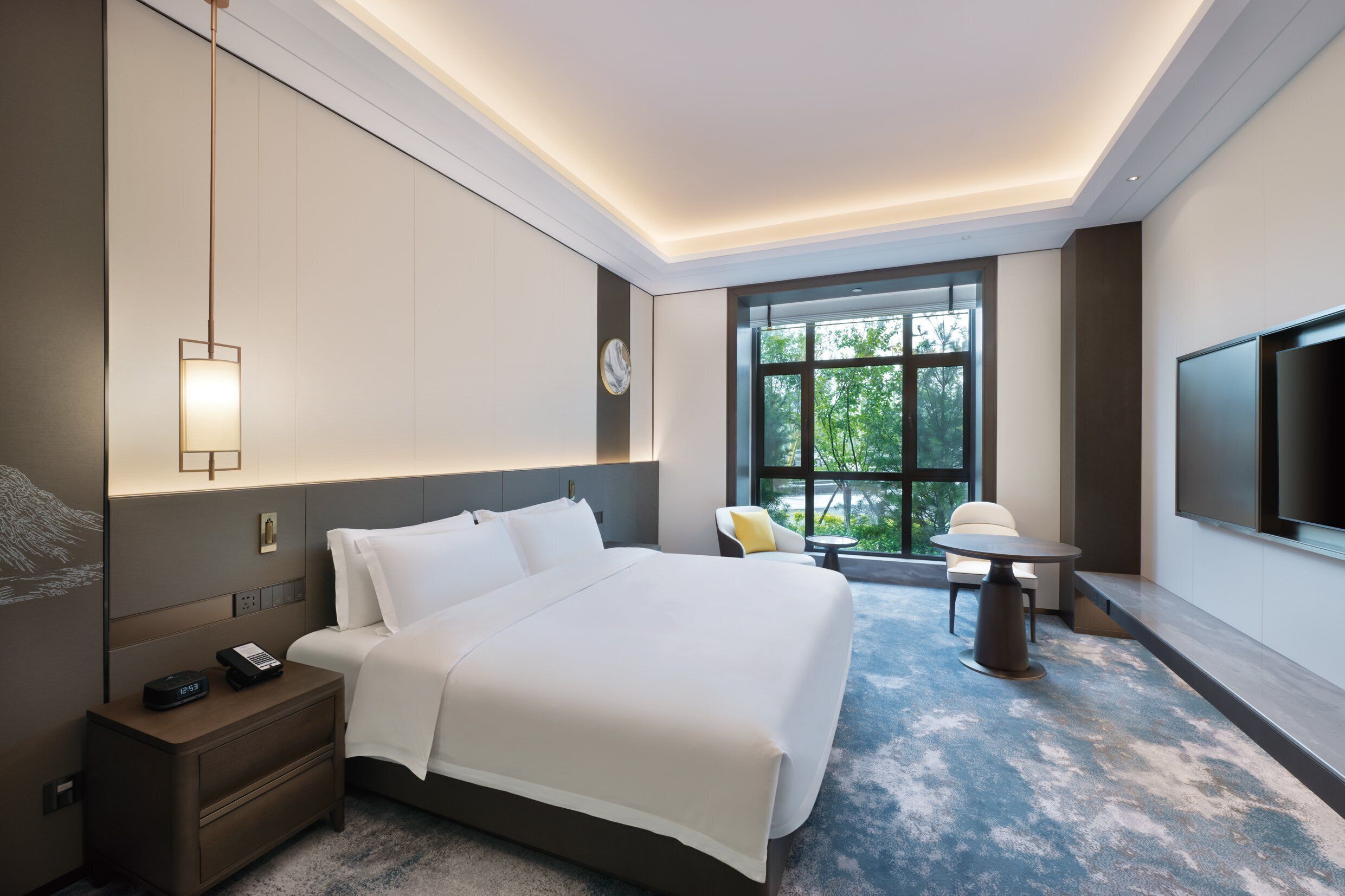 A hotel room with a large bed, bedside table, nightstand, and a TV mounted on the wall.