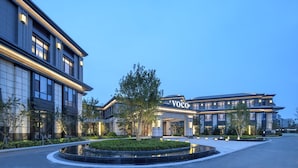 A modern hotel with a large entrance, a well-maintained garden, and a clear sky. - voco Xiongan by IHG (Baoding)