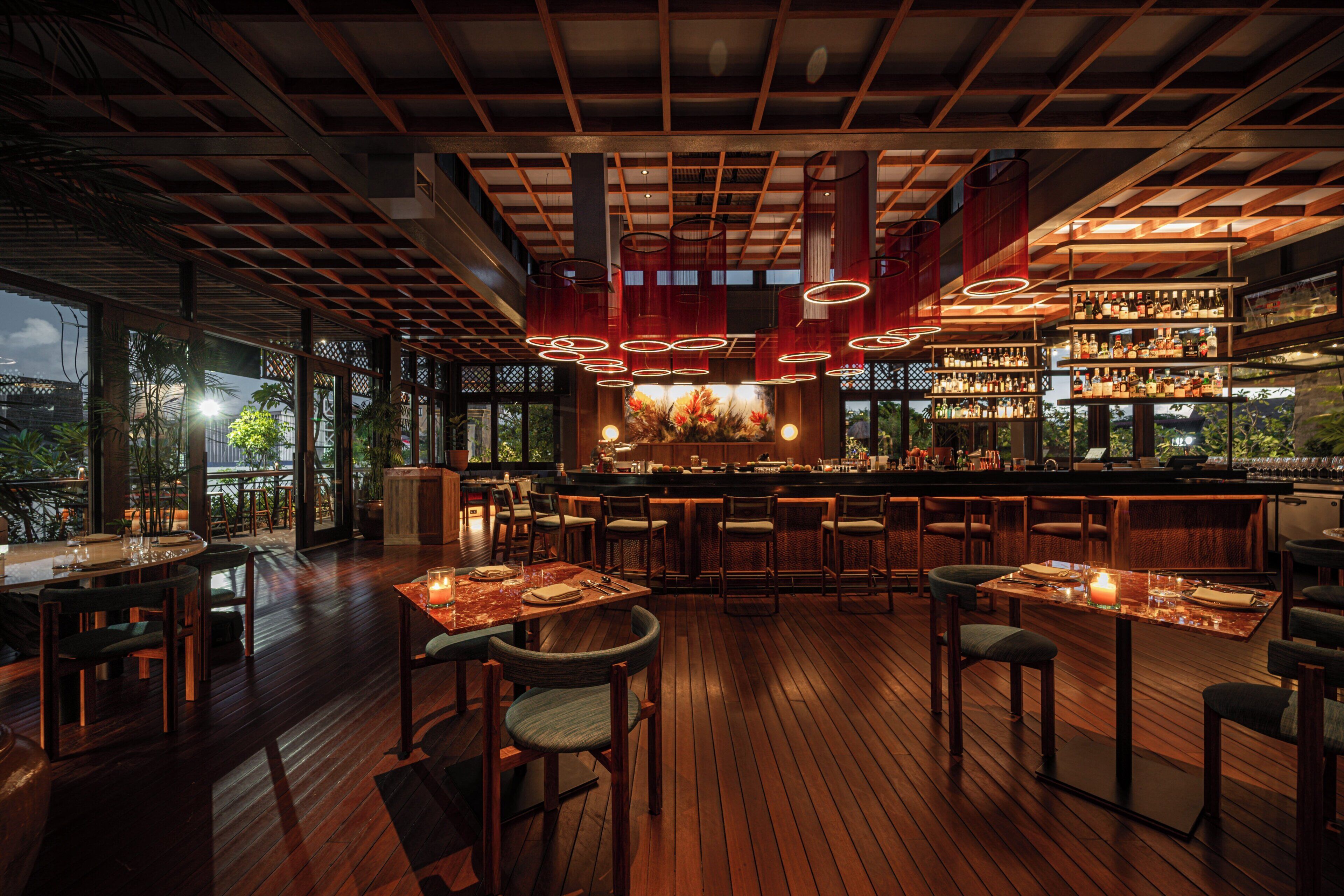 A bar area with wooden flooring, multiple seating arrangements, and a bar stocked with various bottles.