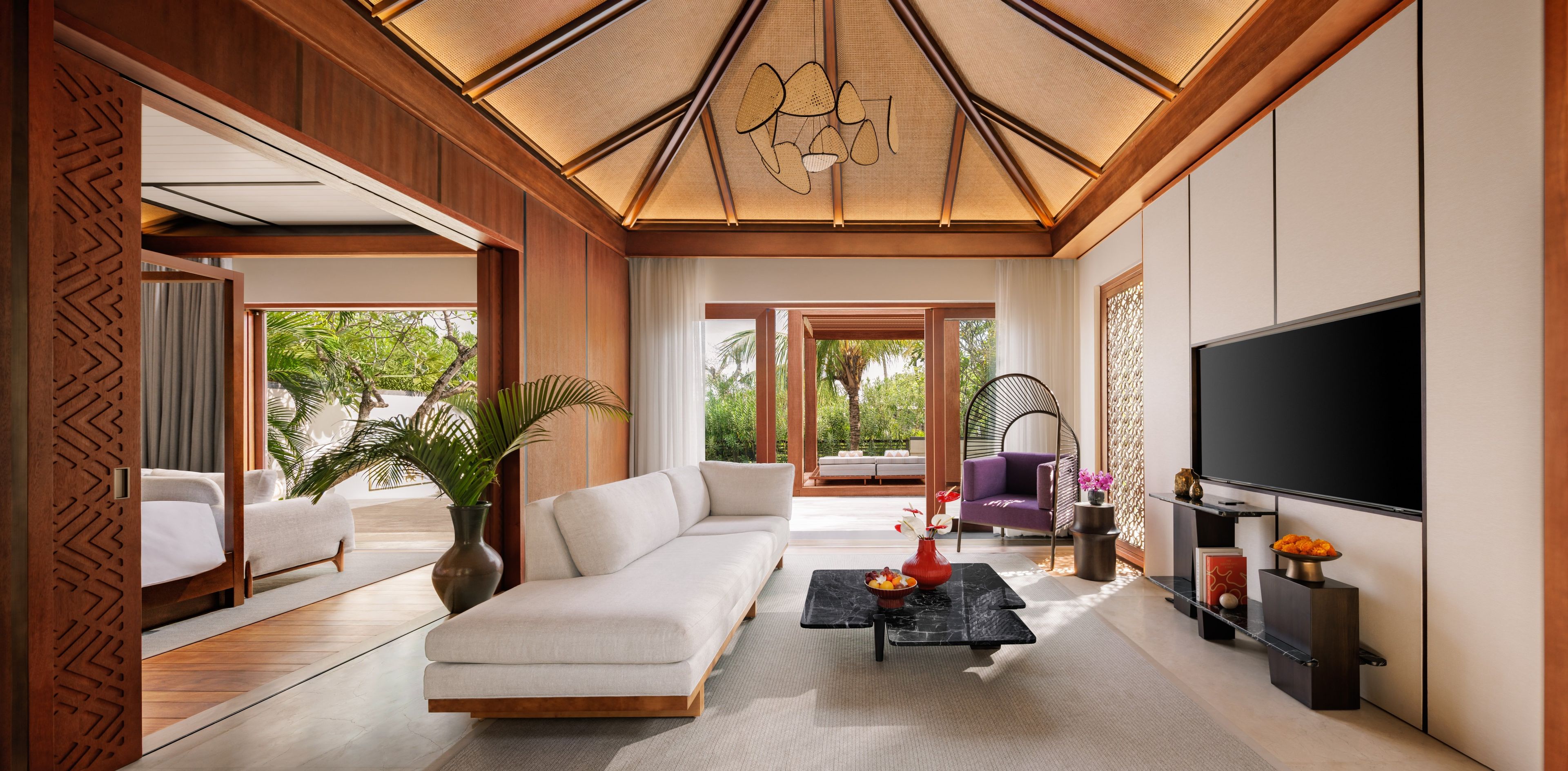 A modern living room with a sofa, a coffee table, a TV, and a large window offering a view of greenery.