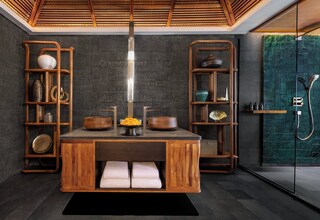 A modern bathroom with a wooden vanity, shelves with decorative items, and a glass shower enclosure.
