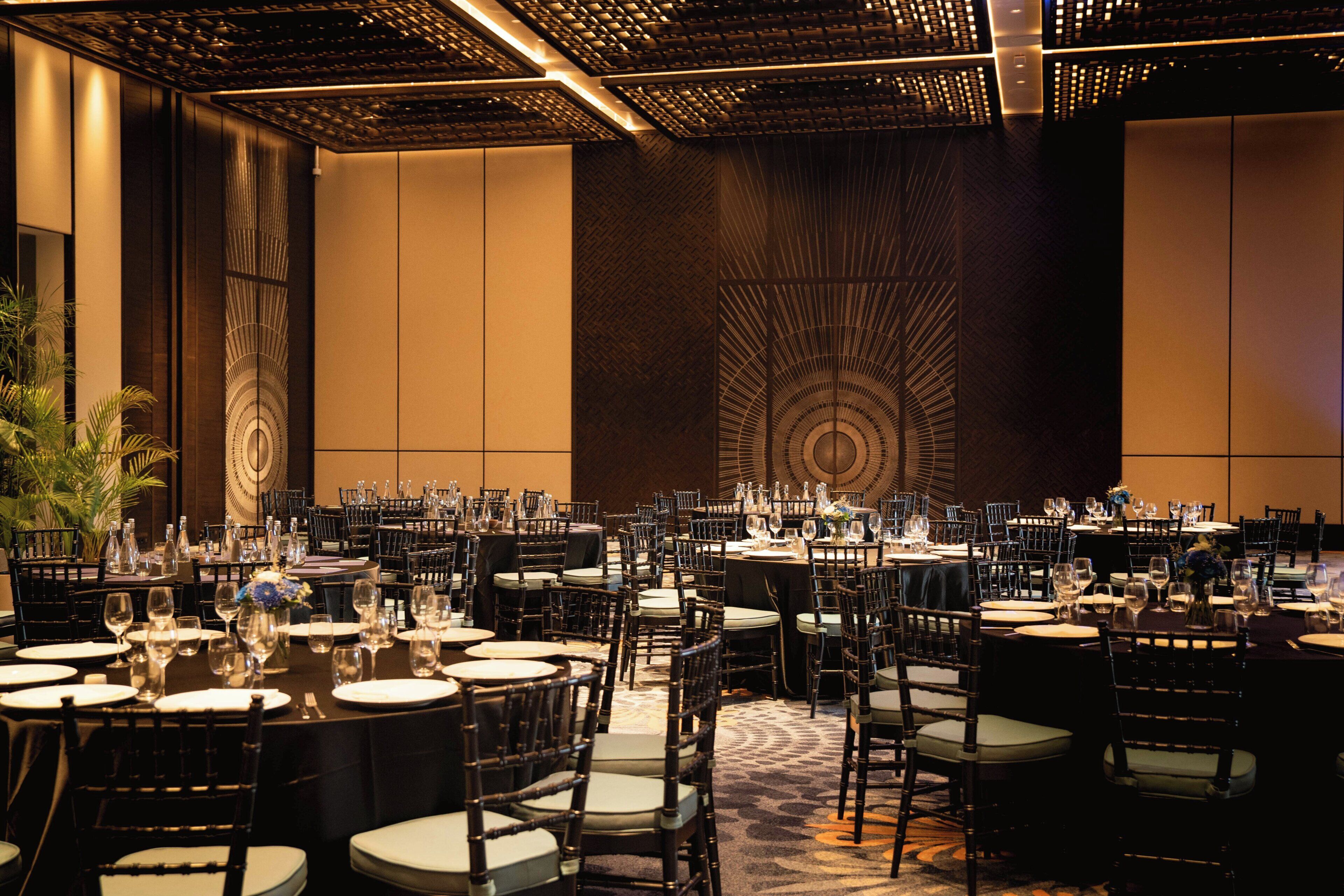 Une salle de banquet avec des tables rondes, des chaises et un mur orné de motifs.