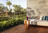 A modern outdoor seating area with a wooden deck, a cushioned sofa with pillows, and a vase of flowers.