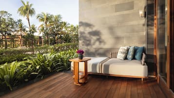 A modern outdoor seating area with a wooden deck, a cushioned sofa with pillows, and a vase of flowers.