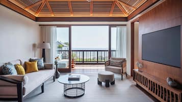 Un salón amplio con sofá, reposapiés y mesa de centro, un televisor montado en la pared, y un balcón con vistas.