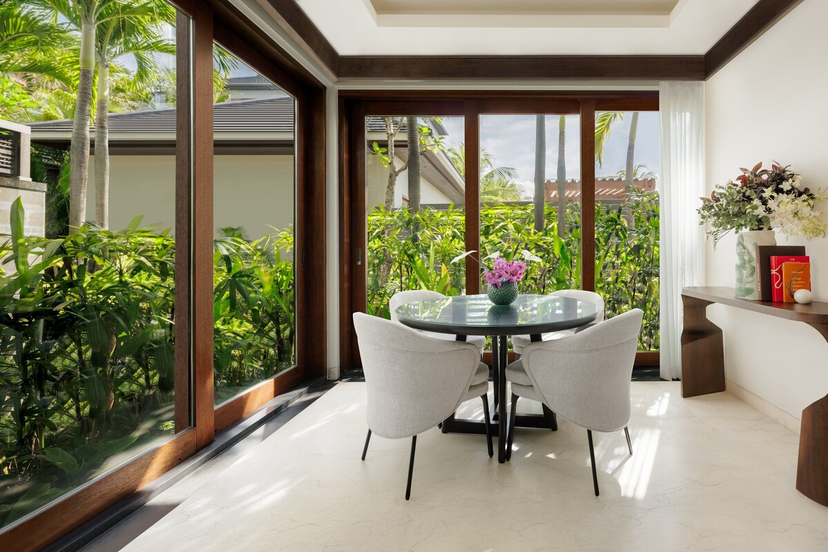 A dining area with a glass table and chairs, a vase with flowers, and a wooden sideboard.