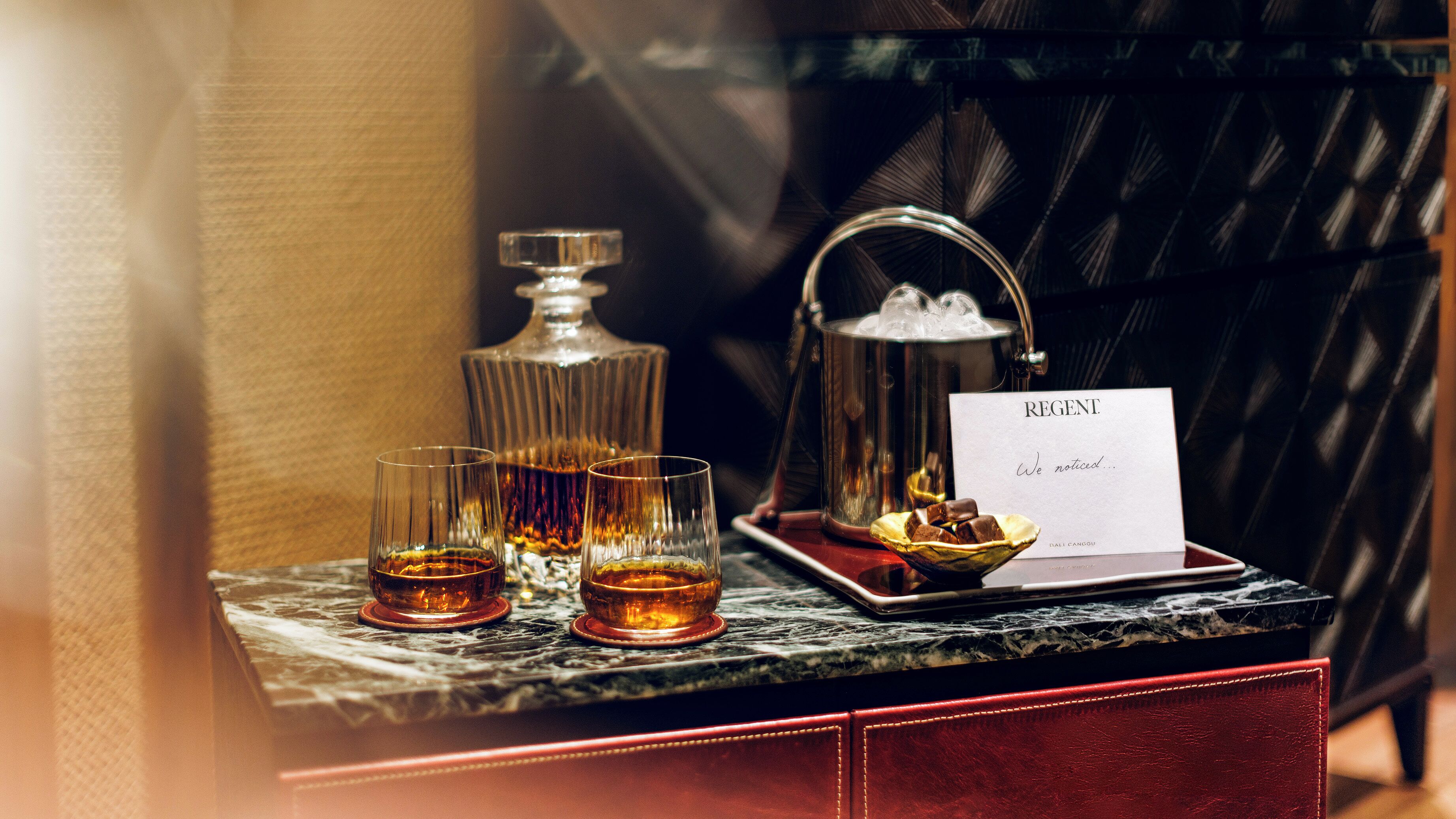 A bar area with a bottle, glasses, and a tray with chocolates.