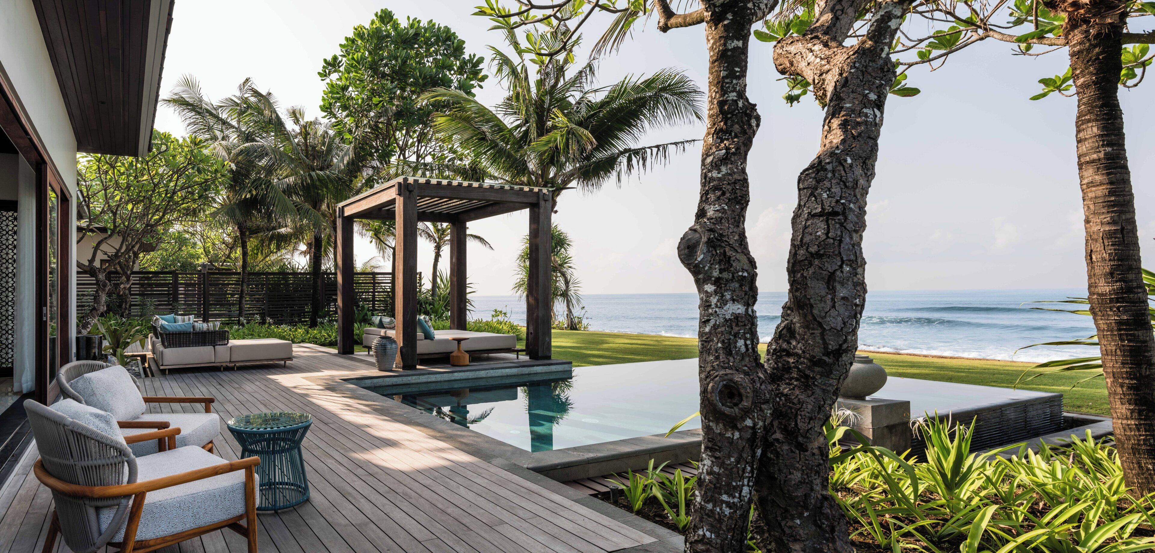 Une terrasse en bois avec une piscine, des chaises longues et une pergola offrant une vue sur l’océan.