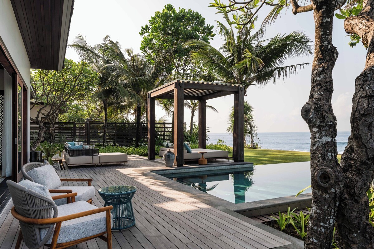 A wooden deck with a pool, lounge chairs, and a pergola overlooking the ocean.