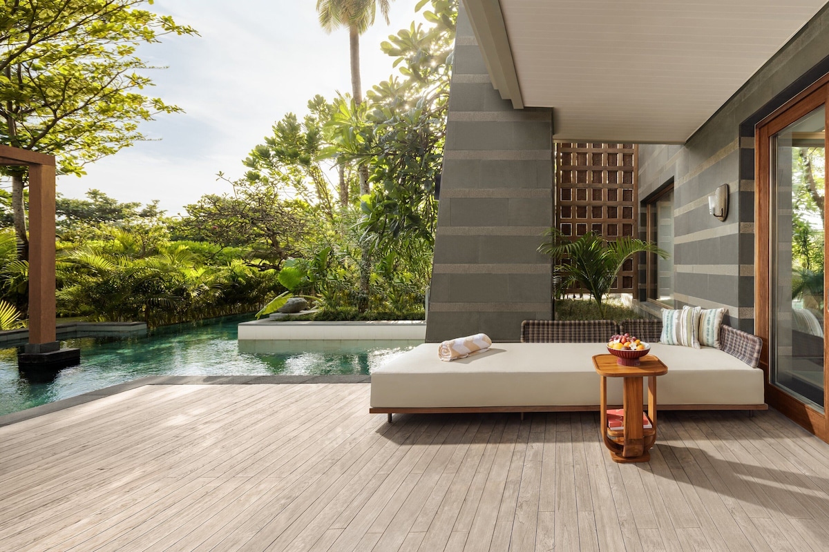 A modern outdoor seating area with a pool, wooden deck, and a glass door leading to a room with a wooden table and a small plant.
