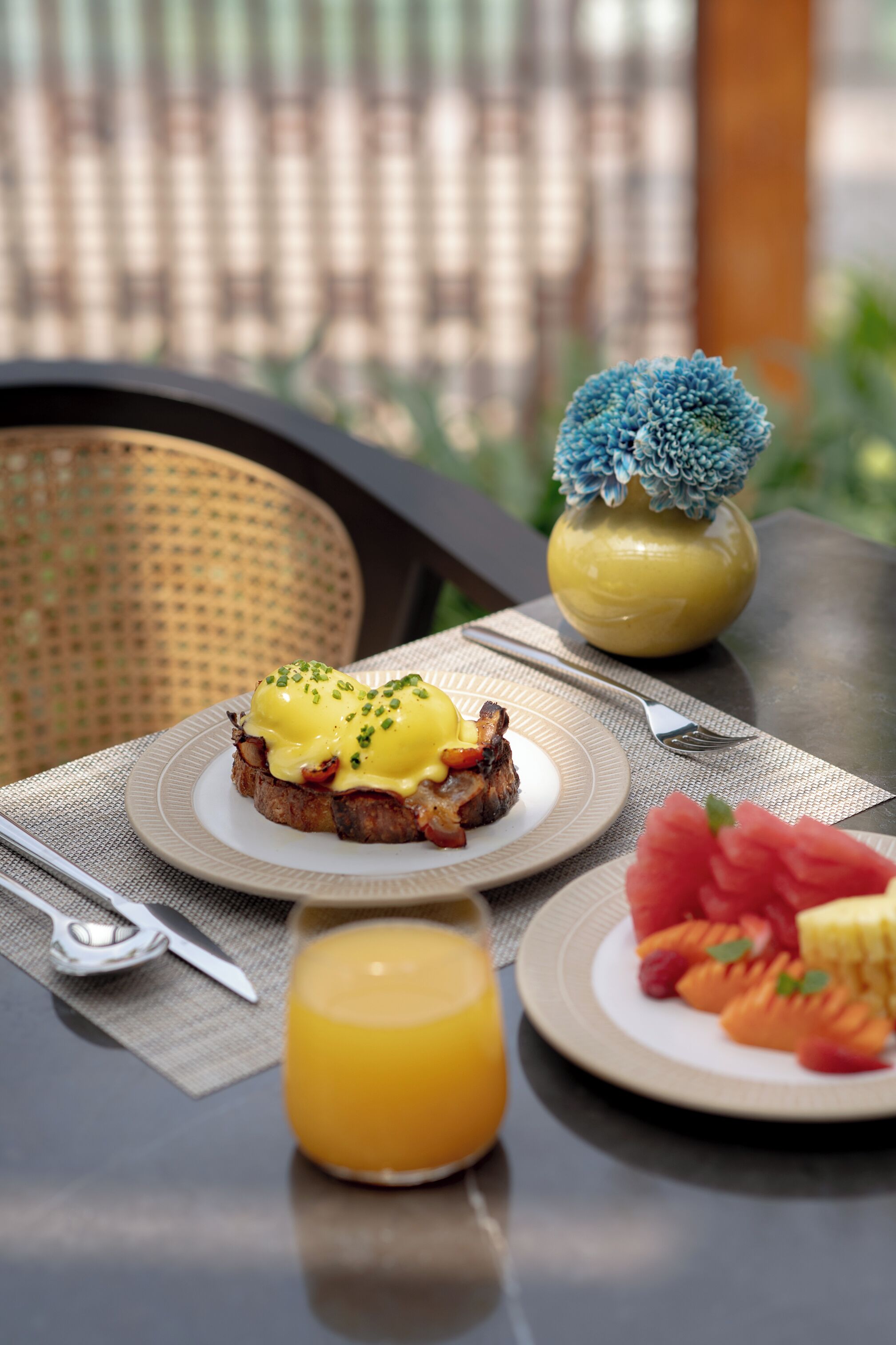 Una colazione con uova alla Benedict, un bicchiere di succo d'arancia e un piatto di insalata di frutta su un tavolo.
