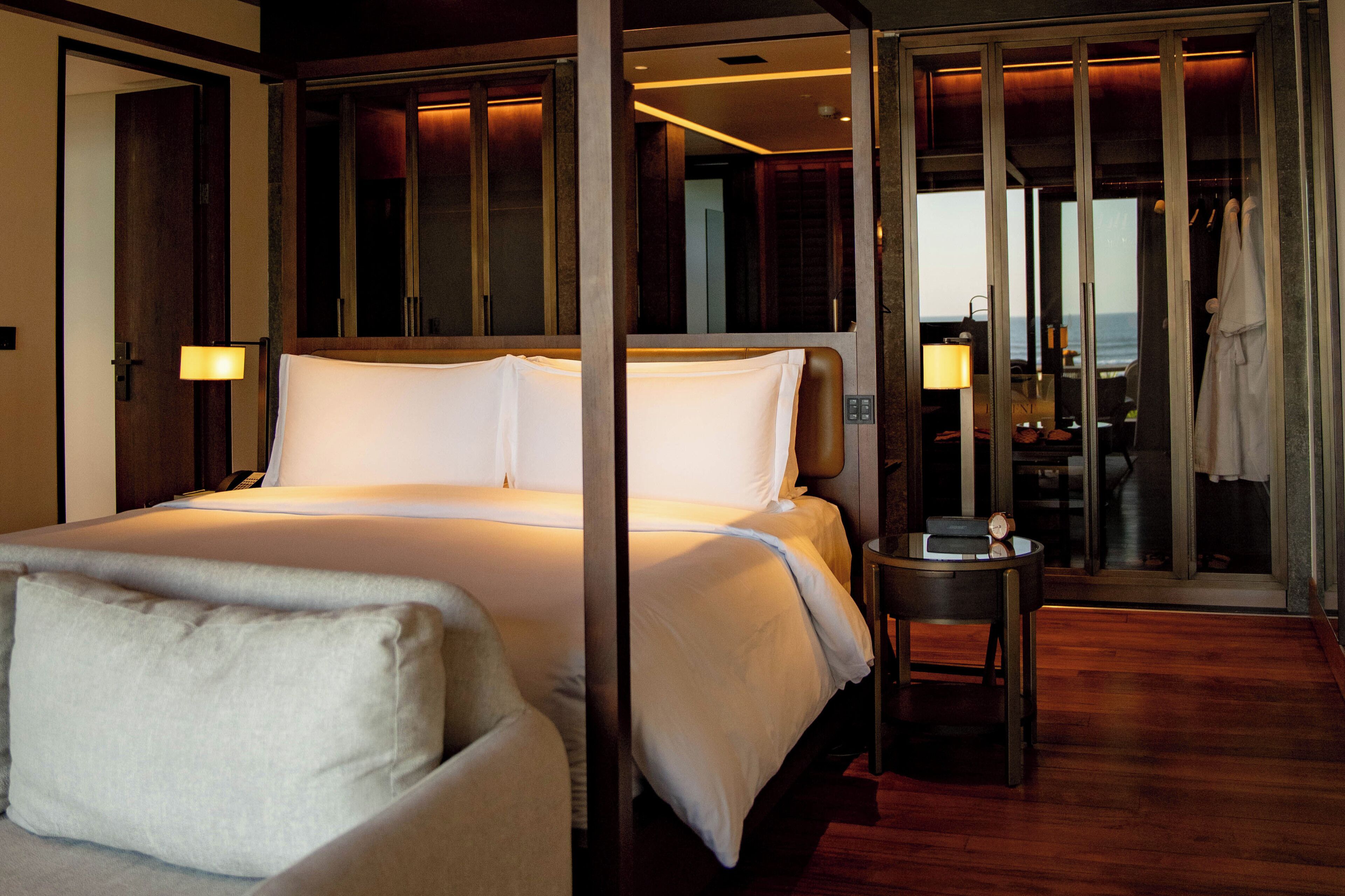 A hotel room with a large bed, a small table, a mirror, and a view of the ocean.