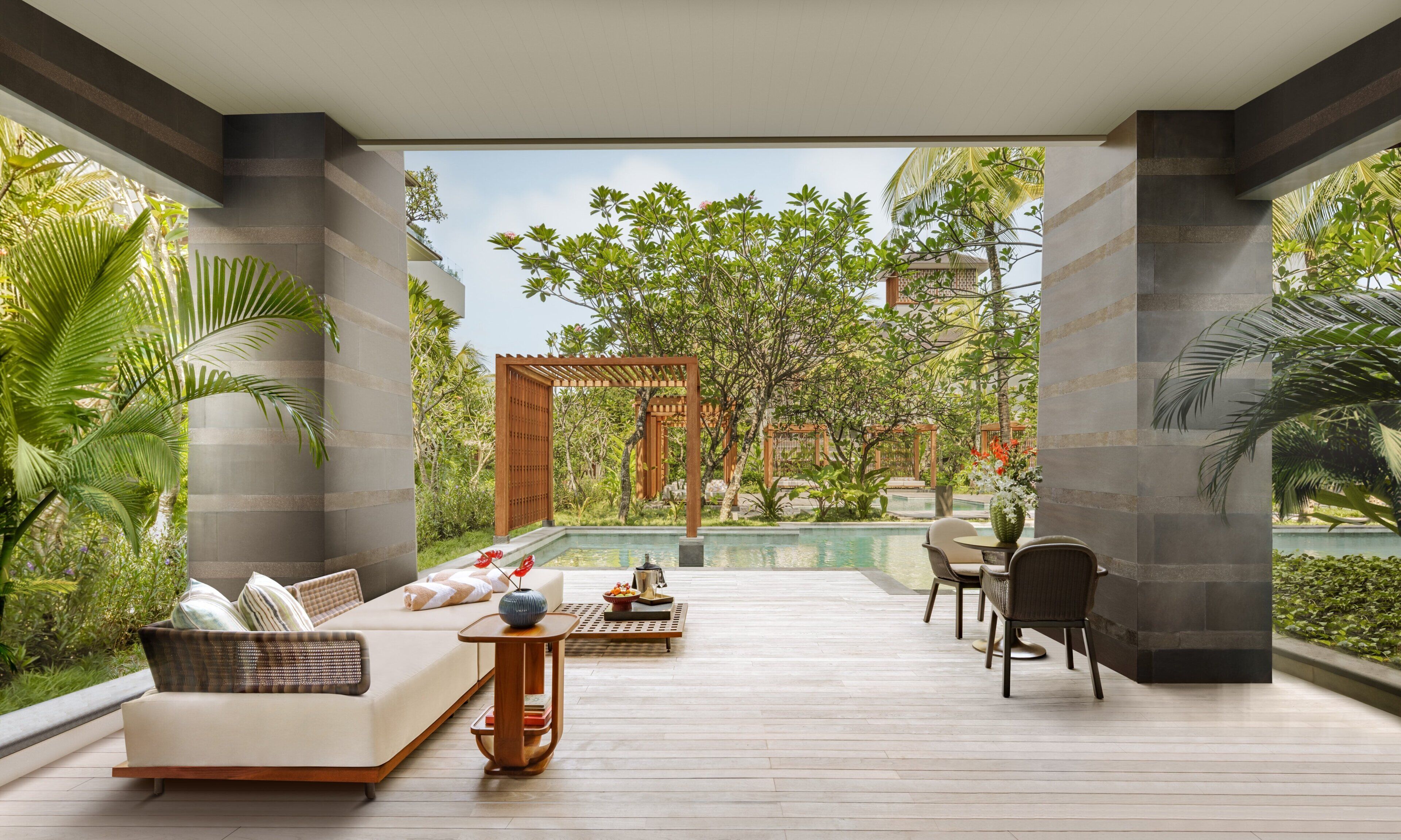 A modern outdoor lounge area with a pool, seating, and lush greenery.