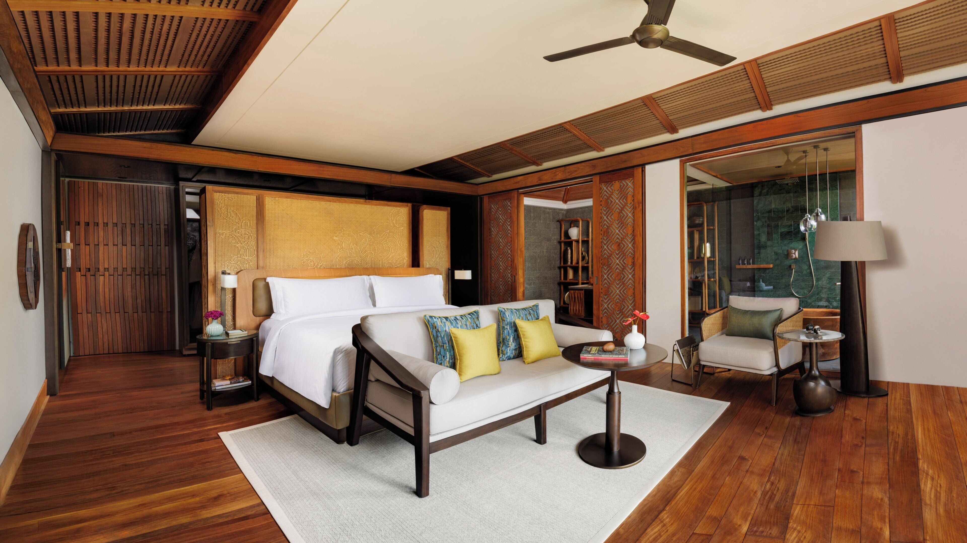 A modern hotel room with a large bed, a sofa, a small table, and a ceiling fan.