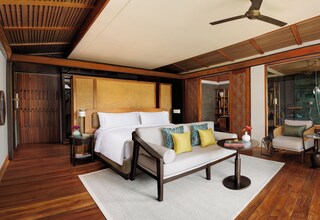 A modern hotel room with a large bed, a sofa, a small table, and a ceiling fan.