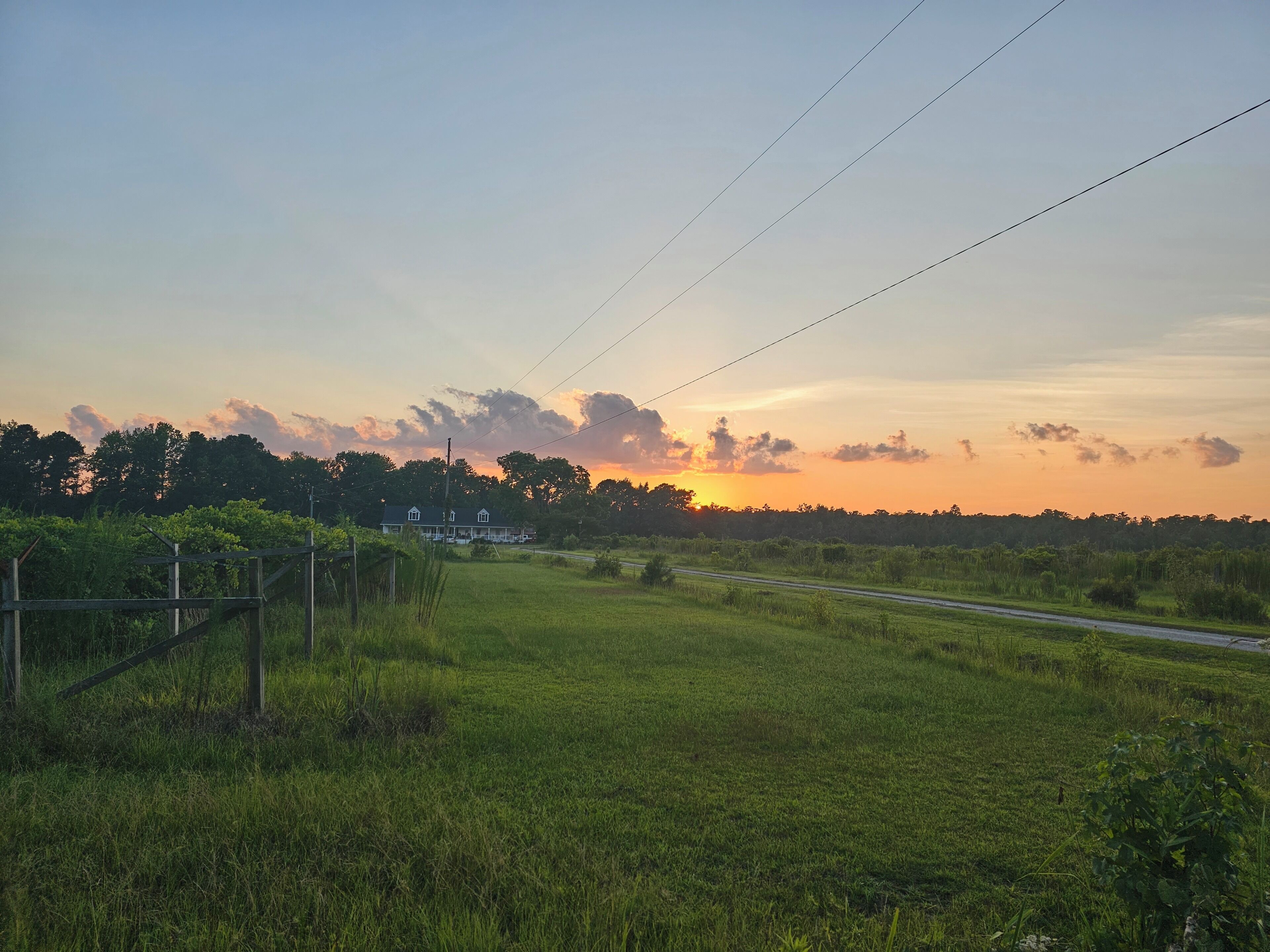 A rural landscape with a road, a house, and a sunset.