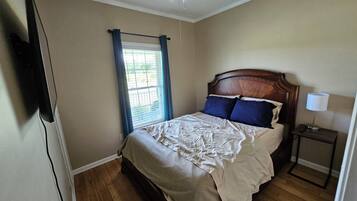 Un dormitorio con una cama de madera, una mesita de noche con lámpara, una ventana con cortinas y un ventilador de techo.