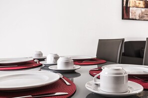 A dining table set with plates, bowls, and cups, accompanied by red placemats and silverware. - Portside Lodge Building (Marsaskala)