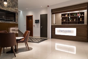 A modern lobby with a reception desk, a staircase, and a dining area with chairs and a table.
