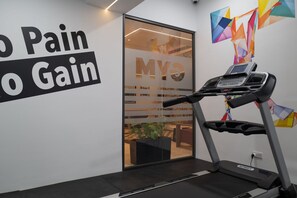 A treadmill in a room with a motivational wall sign reading "Pain No Gain" and a logo "Myo".
