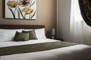 A hotel room with a large bed, a nightstand, a lamp, and a painting of flowers on the wall.