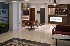 A modern hotel lobby with a reception desk, seating area, and a large mirror. - Portside Lodge Building (Marsaskala)